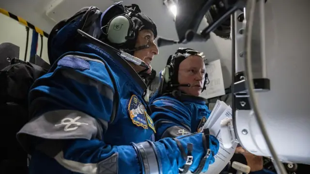 Astronotlar Suni Williams (solda) ve Butch Wilmore mavi kıyafetleri içerisinde Starliner kapsülünün kokpitinde oturuyor.